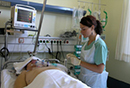 Am Bett eines Patienten auf der Intensivstation steht eine junge Krankenpflegerin und gibt Infusion.